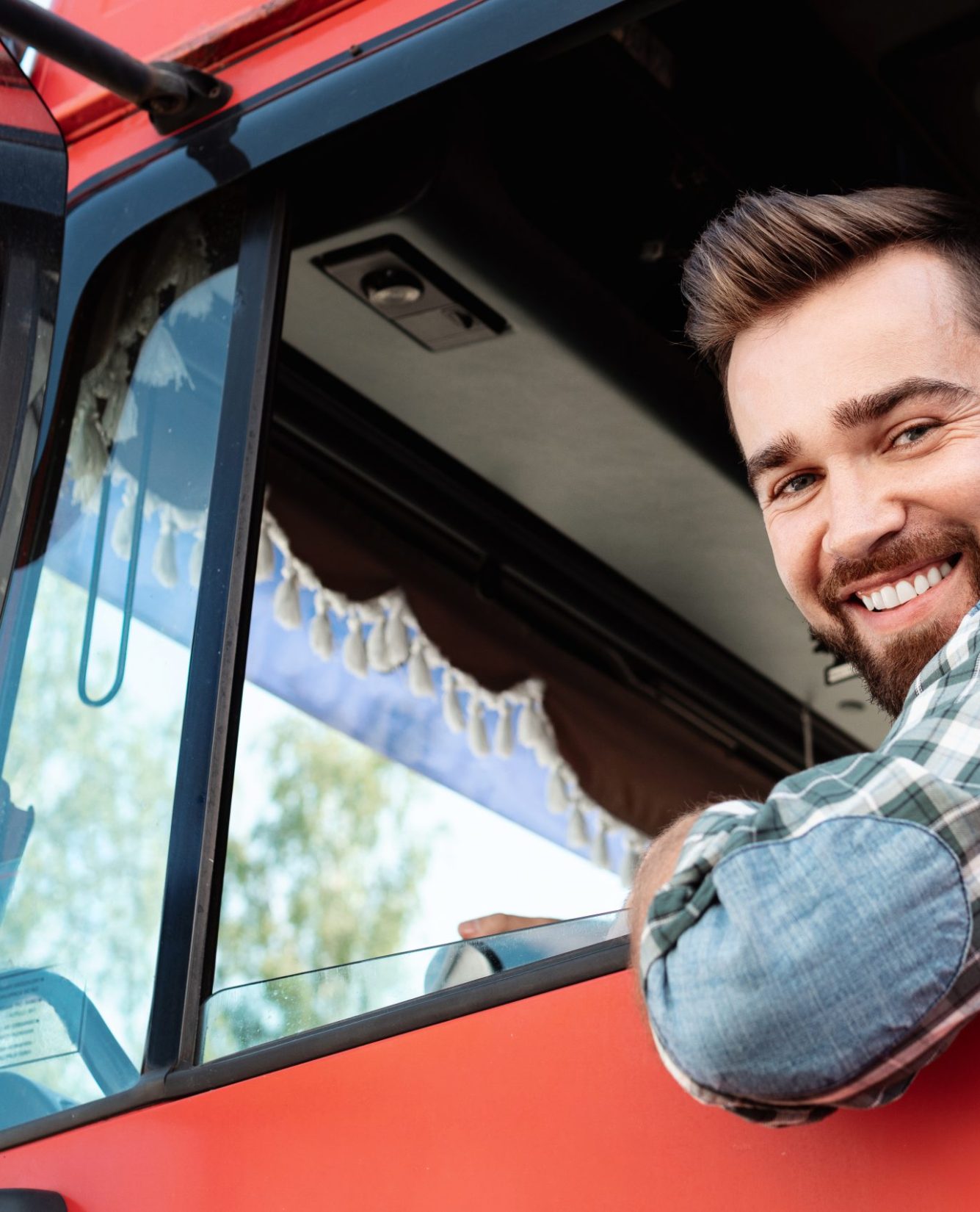 Young and happy male truck driver inside his red cargo truck